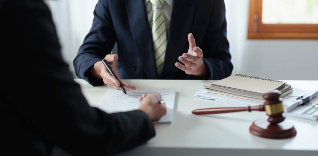Lawyer consulting client with legal documents, gavel and notepad on a white desk in office