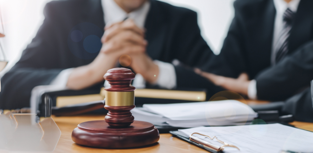 Close-up of a judge’s gavel on a desk with two lawyers in suits discussing legal documents