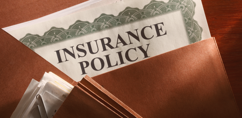 Close-up of an insurance policy document partially visible inside a brown folder on a wooden desk