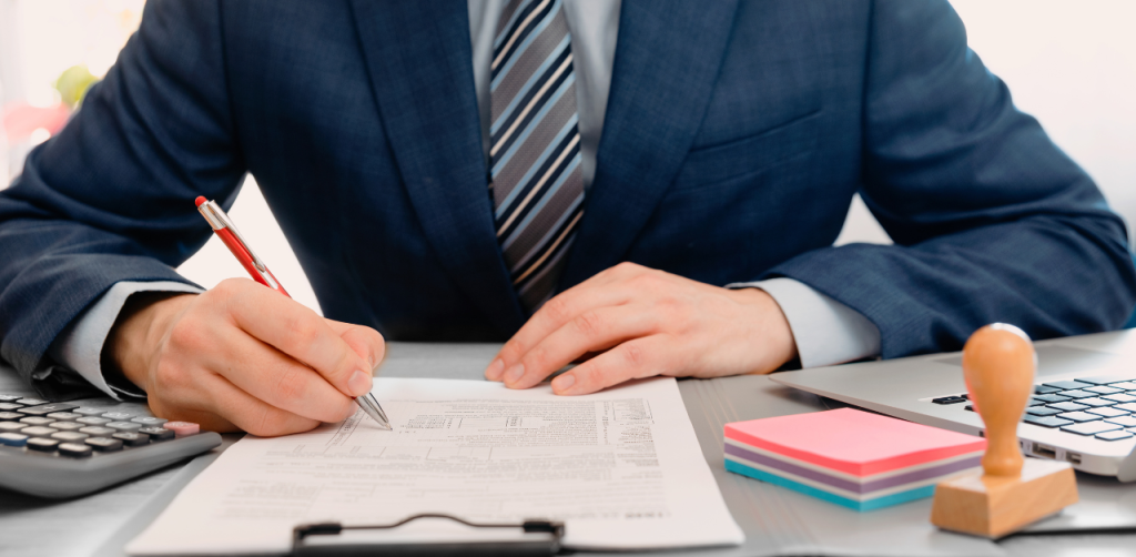 Businessman in suit filling out legal or financial paperwork at a desk with office tools