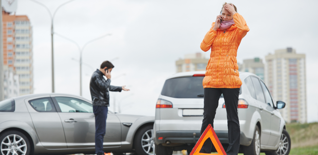 Two drivers on phones after a car accident, with warning triangle placed in front