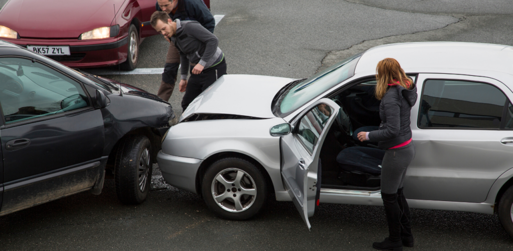 Two damaged cars after a collision, with people inspecting the scene