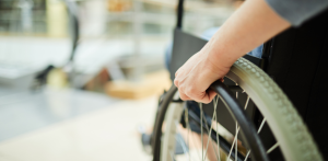 Close-up of a person's hand gripping the wheel of a wheelchair, with a blurred background