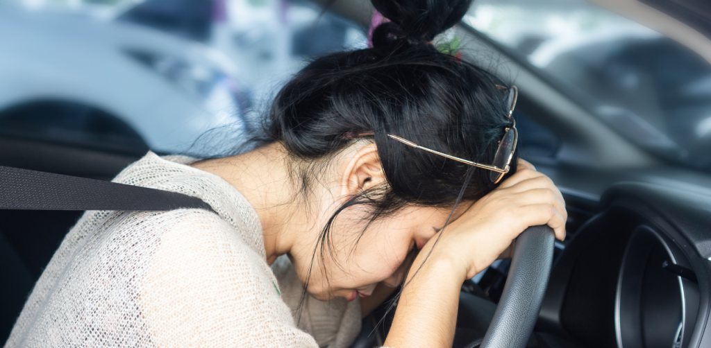 Frustrated woman in a car rests her head on the steering wheel, overwhelmed or stressed while driving