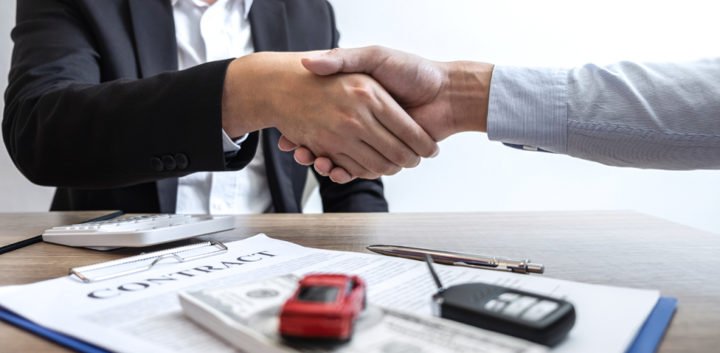 Two people shake hands over a car contract, symbolizing a successful auto sale or lease deal