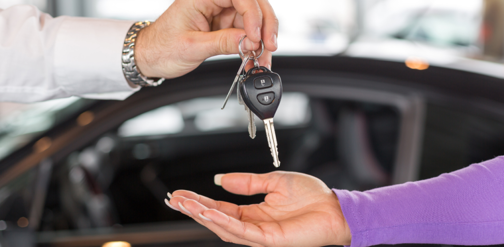 Person hands over car keys to new owner at a dealership, highlighting vehicle transfer