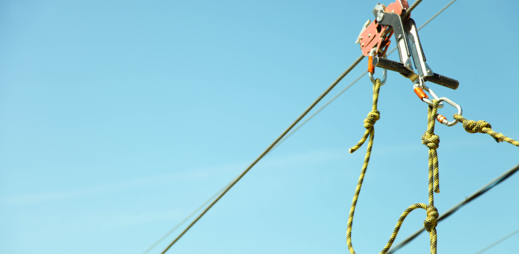 Close-up view of a zip line pulley and safety harness system suspended against a bright blue sky, highlighting the importance of secure equipment in zip line safety