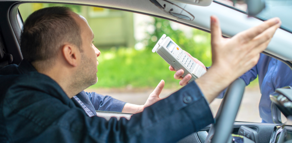 Driver inside car reacts as police officer holds a breathalyzer through the window