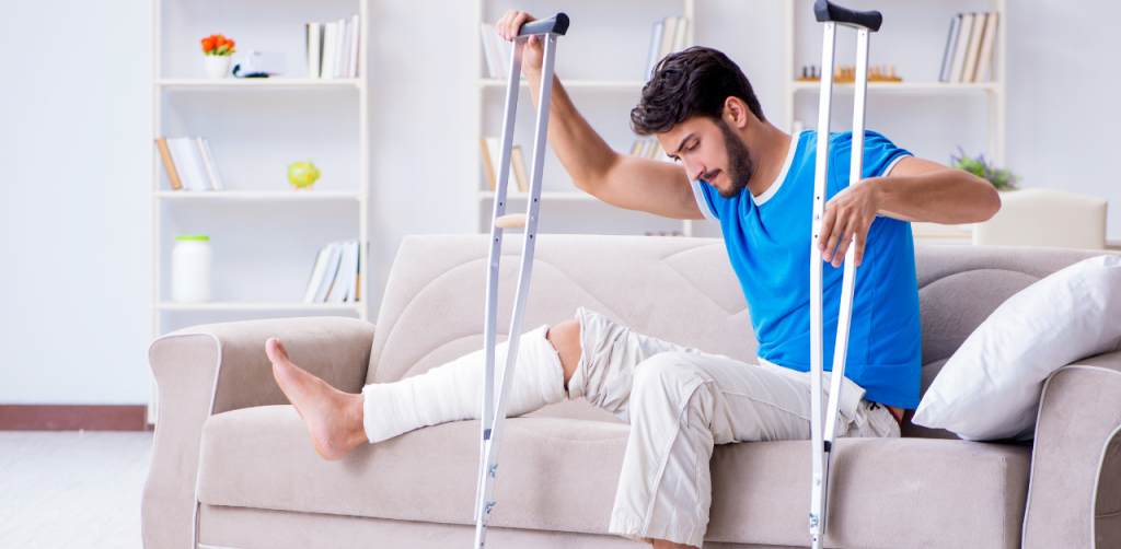 Injured man with crutches and leg cast sits on couch, recovering from a motorcycle accident