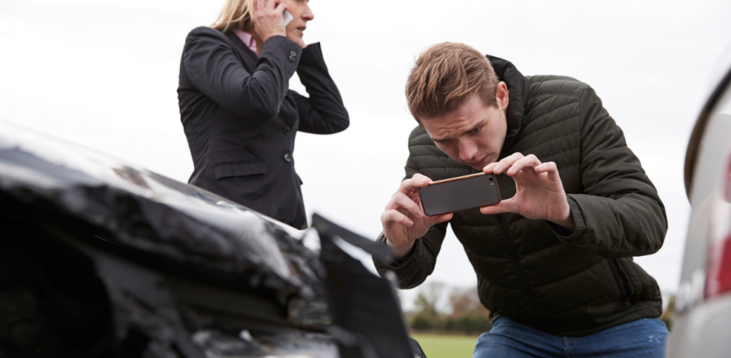 Woman talking on the phone and man taking pictures to a car crashed