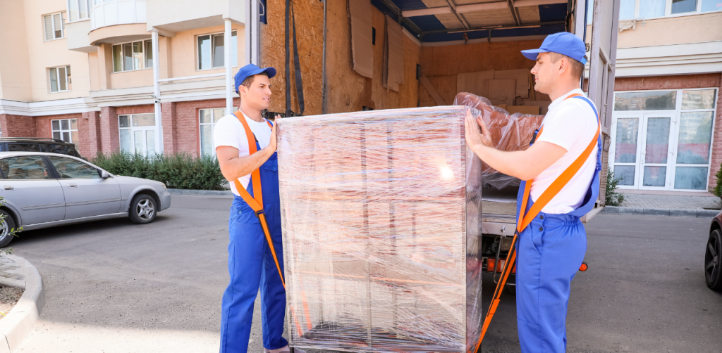 Two movers unloading a large wrapped item from a moving truck