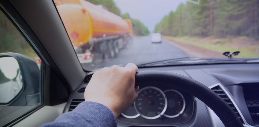 Driver’s view from inside a car on a highway, passing a fuel tanker truck on a rainy forest road