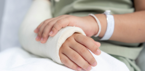 A child with a hospital wristband rests their hand on a cast-covered forearm, suggesting injury care