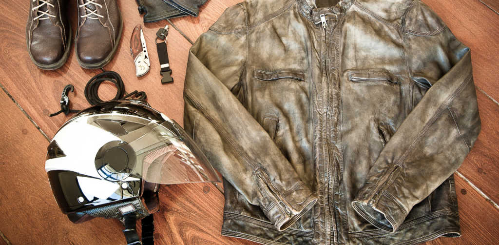 Biker gear laid out on a wooden floor, including a leather jacket, helmet, boots, and accessories