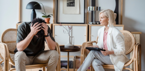 Man holding his head in frustration while speaking with a female therapist in an office