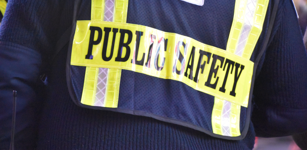 Close-up of a high-visibility vest labeled “PUBLIC SAFETY,” worn by emergency or safety personnel