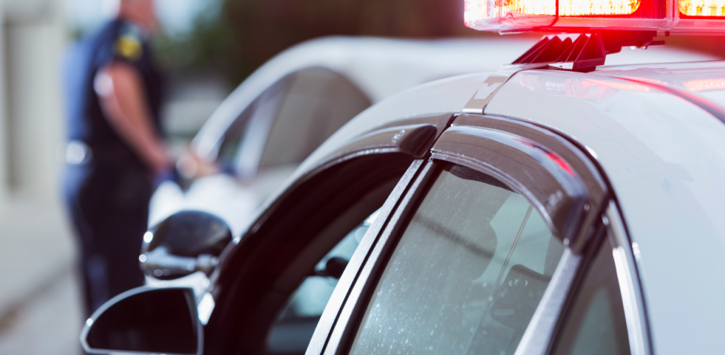 Police Traffic Stop - A police car with flashing lights, as an officer approaches a stopped vehicle