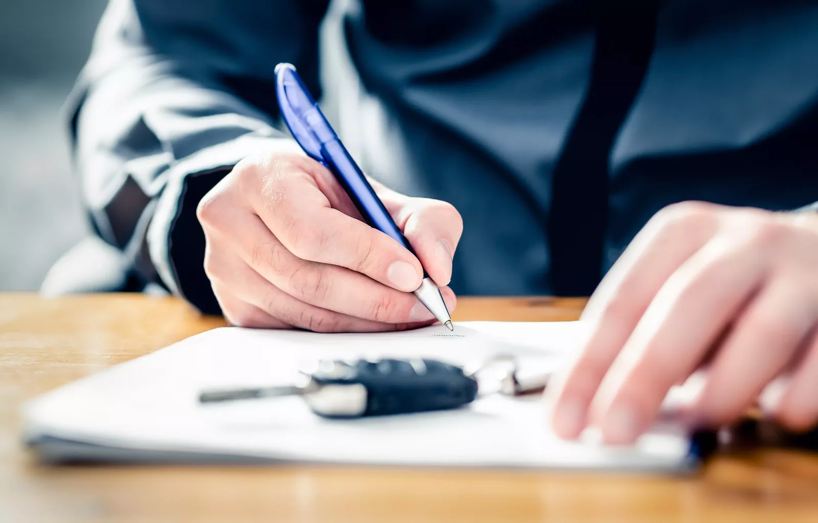 Signing loan financing paperwork with car keys on the desk