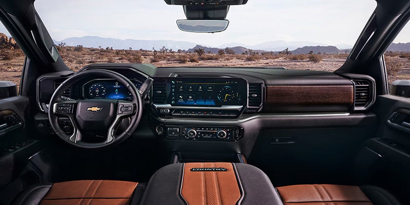 Interior view of a modern car dashboard with a steering wheel, digital displays, brown leather seats, and a desert landscape visible.