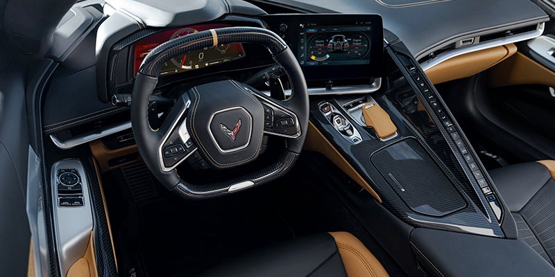 Modern car interior with black and tan accents, a steering wheel, digital dash, infotainment screen, and controls.