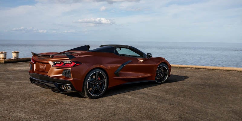 Bronze convertible Corvette C8 parked on a pier, with the ocean and cloudy sky in the background.