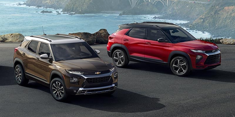 A gold, and a red Chevy Trailblazer are shown parked in front of the ocean.