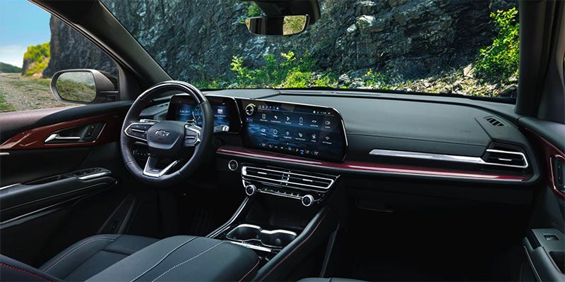 Interior view of a modern car cockpit with digital screens, a steering wheel, and a rocky, green landscape outside.
