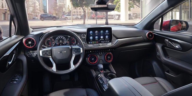 Car interior showing a black dashboard, steering wheel, digital gauges, and infotainment screen with red accents.