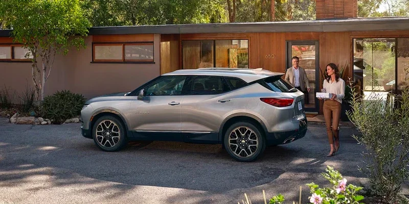 Silver SUV parked in a modern house's driveway, as a man and woman walk out with a package.