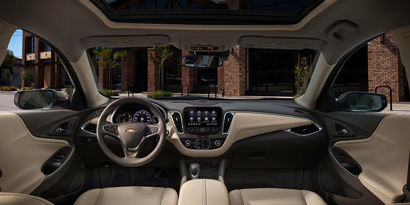 View from inside a modern car, showing the dashboard, steering wheel, infotainment screen, and light tan interior.