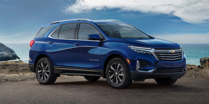 Blue Chevrolet Equinox SUV parked on a road overlooking the ocean under a blue sky.