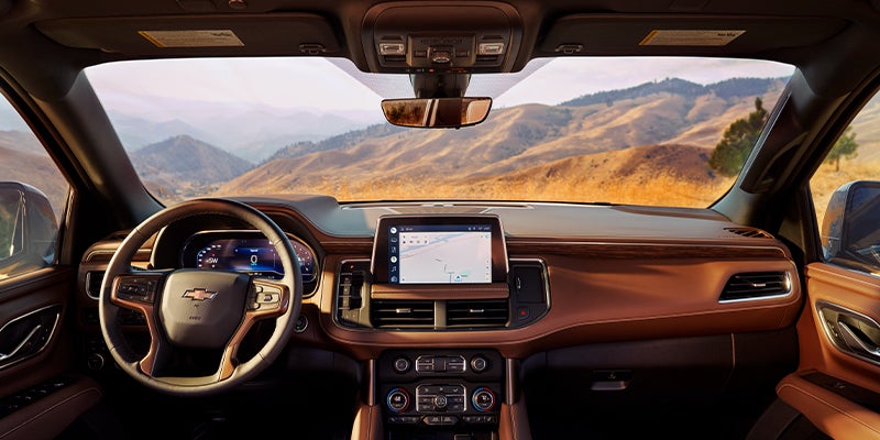 Car interior with brown dashboard, steering wheel, digital displays, and navigation screen, overlooking mountains.