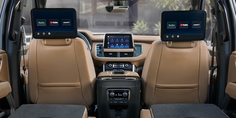 Car interior with tan leather seats, two rear-seat entertainment screens, and a center console.