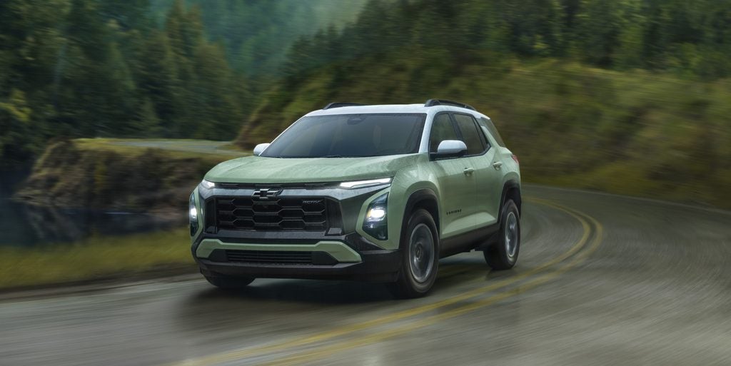 Light green Chevrolet Trax ACTIV SUV driving on a wet, winding road through a blurred forest.