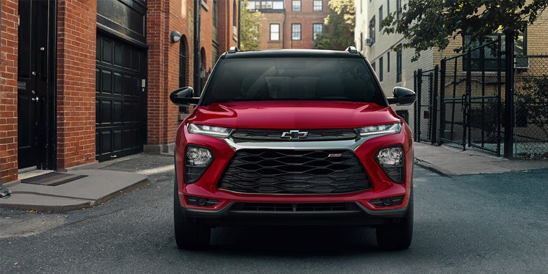 Red Chevrolet Trailblazer SUV parked head-on in an urban alleyway between brick buildings.