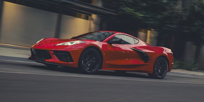 Red Chevrolet Corvette C8 sports car speeding on a street, blurred background suggesting motion.