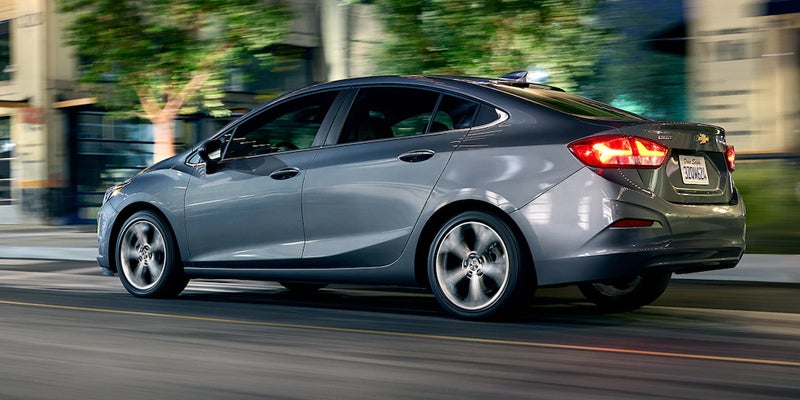 Gray Chevrolet Cruze sedan driving at night on a street, with illuminated taillights and motion blur.