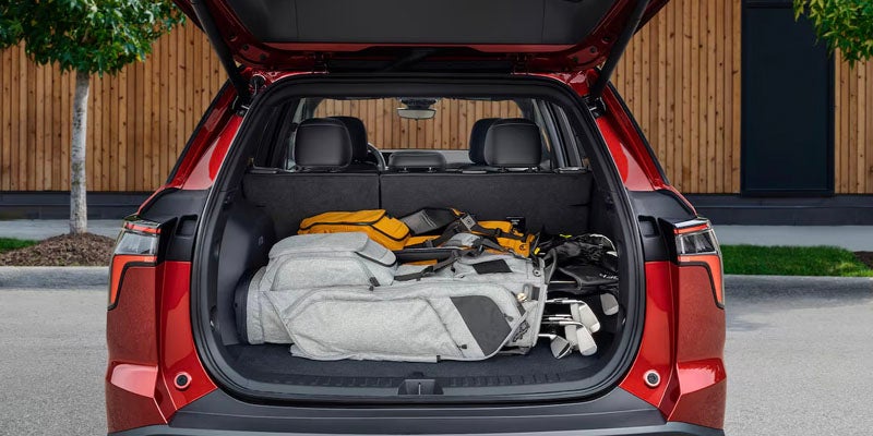 Open trunk of a red SUV filled with a grey golf bag, a yellow bag, and golf clubs.