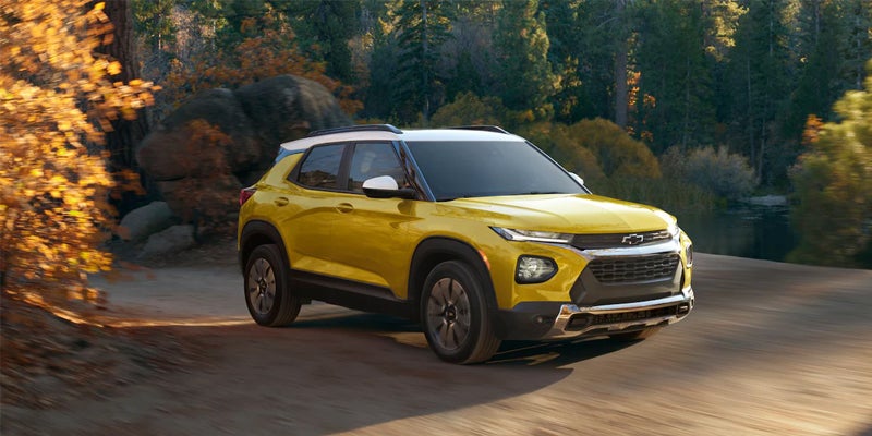 Yellow SUV with a white roof driving on a dirt road through an autumn forest.