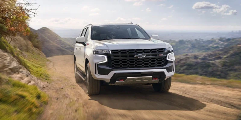 White Chevrolet SUV driving on a dirt road through mountainous terrain, with motion blur on the road.