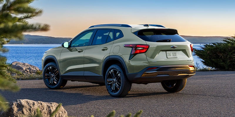 Light olive green SUV parked on an asphalt road overlooking a vast blue lake at sunset.