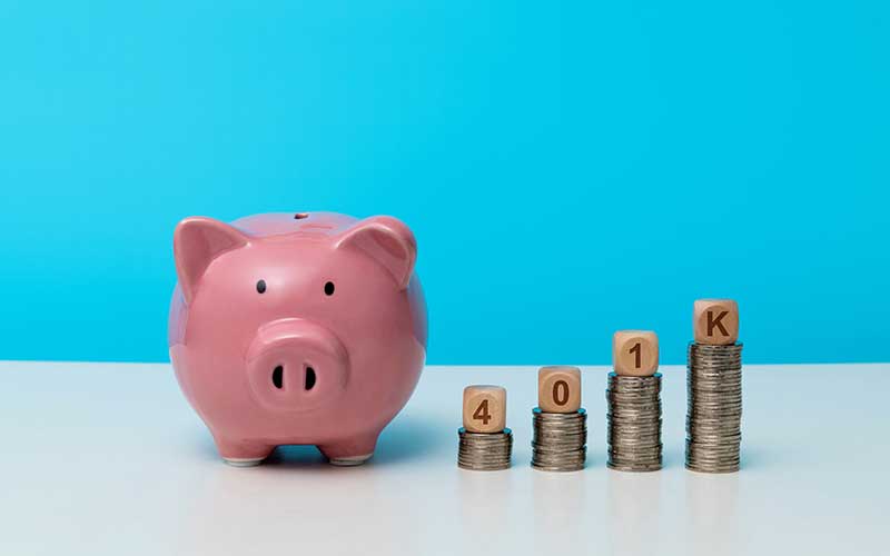 Pink piggy bank next to growing stacks of coins, topped with wooden blocks spelling 401K.