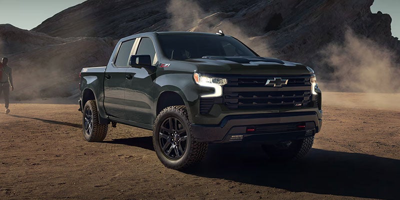 Dark green Chevrolet Silverado Z71 pickup truck parked on a dirt road in a desert landscape with a person walking.