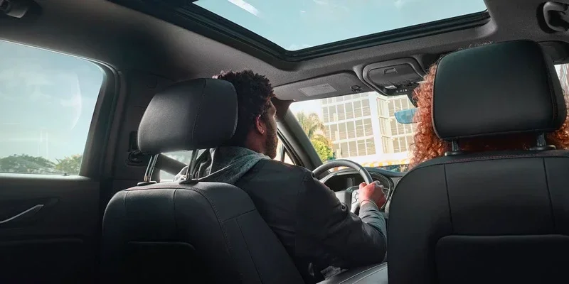View from back seat of a car showing a man driving, a woman in the passenger seat, and a sunroof.