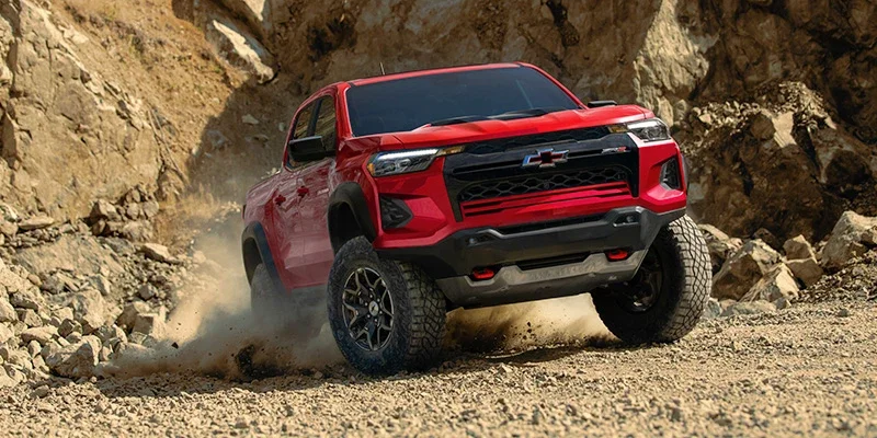 Red Chevy Colorado ZR2 pickup truck off-roading on a rocky, dusty dirt path.