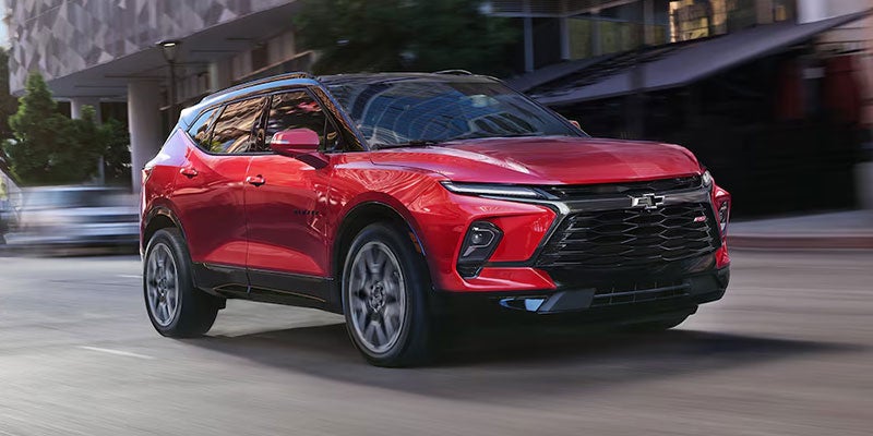 Red Chevrolet Blazer SUV driving on a city street with blurred background.