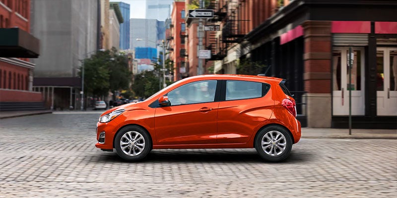 Orange Chevrolet Spark hatchback driving through an urban street with motion blur in the background