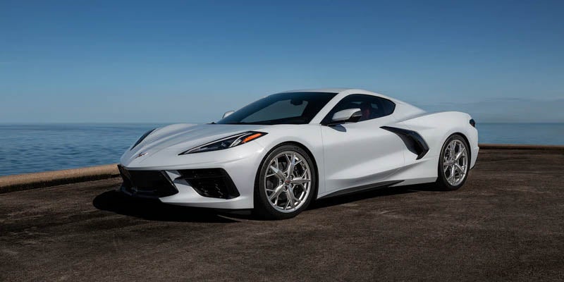 White sports car parked by calm blue water under a clear sky.