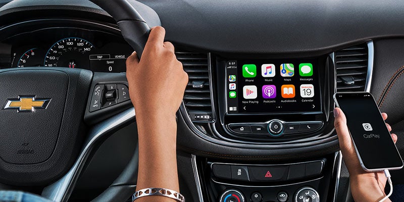 Vehicle infotainment touchscreen and dashboard controls with a hand interacting with the display.