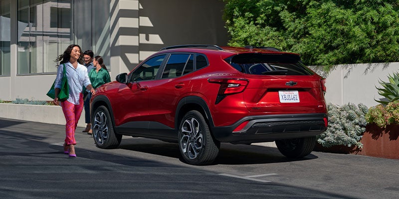 A red SUV parked outside with three people walking towards it, one woman smiling in the foreground.